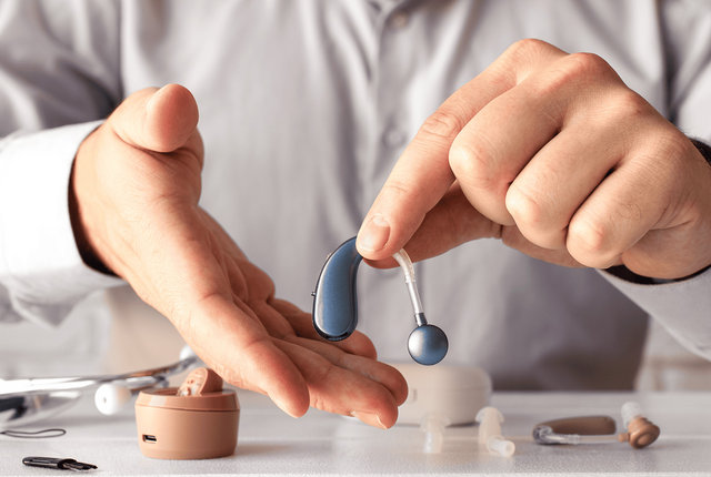 Akustiker zeigt modernes Hörgerät – NOVENTI Abrechnungsservice für Hörakustik-Betriebe.