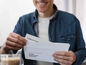 Mann öffnet einen Brief mit einer Rechnung, der per Post von NOVENTI kommt.