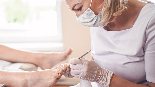Podologin führt eine Nagelspangenbehandlung am Fuß einer Patientin durch – therapeutische Versorgung im Rahmen der Heilmittelversorgung.