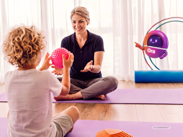 Ergotherapeutin therapiert Kind in der Praxis. Im Vordergrund NOVENTI Ora Character.
