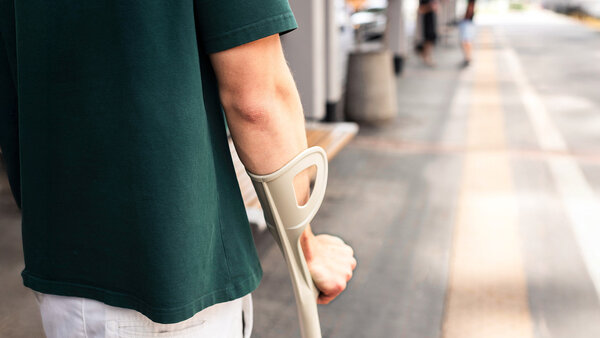 Person mit Unterarmgehstütze wartet auf dem Gehweg – Symbolbild zur Abrechnung von Hilfsmittelrezepten über die Berufsgenossenschaft