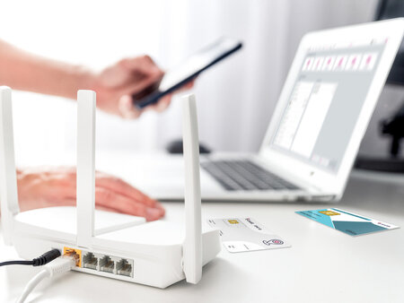 Therapeut arbeitet am Notebook mit Hilfe eiens Smartphones, im Vordergrund steht ein Rooter – Symbolbild für NOVENTI Ti-Begleitservice