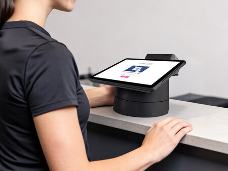 Eine Frau steht an einem Empfangstresen und nutzt ein Tablet auf Halterung zur Dateneingabe bei der Software MyYolo.