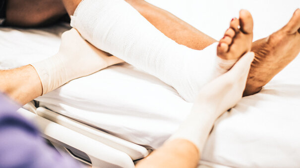 Arzt hilft einem Patienten mit einem gebrochenen Bein – Symbolbild für Physiotherapie - Tipps zur Abrechnung mit einem Unfallversicherungsträger