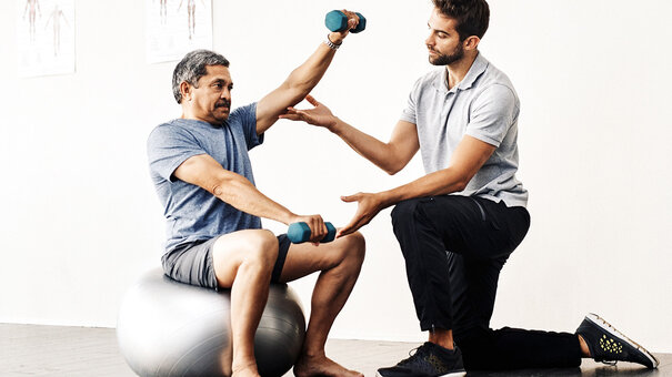 Physiotherapeut unterstützt älteren Patienten beim Training mit Hanteln – Symbolbild für moderne Physiotherapiepraxis und Vorbereitung auf die Telematikinfrastruktur-Förderung.
