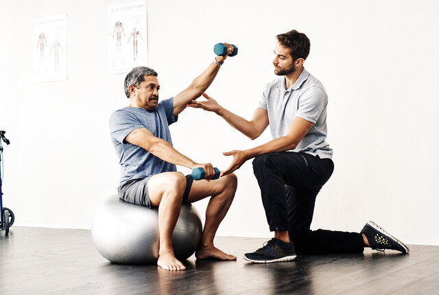 Physiotherapeut unterstützt älteren Patienten beim Training mit Hanteln – Symbolbild für moderne Physiotherapiepraxis und Vorbereitung auf die Telematikinfrastruktur-Förderung.