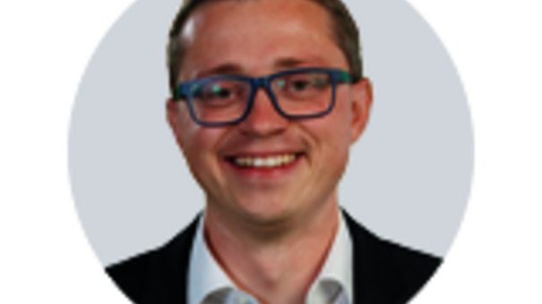 Porträtaufnahme von Sales Manager Steffen Kreisig mit kurzer Frisur, Brille und dunklem Blazer vor neutralem, hellem Hintergrund.
