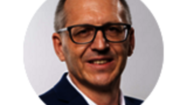 Porträtaufnahme von Sales Manager Dirk Geitner mit kurzer Frisur, Brille und dunklem Sakko vor neutralem, hellem Hintergrund.