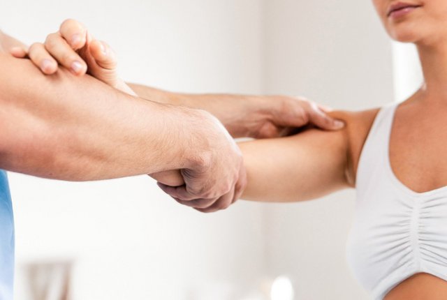 Seitenansicht eines männlichen Physiotherapeuten, der das Schultergelenk einer Patientin überprüft – Symbolbild für Aktuelle Preislisten Physiotherapie