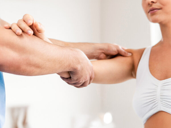 Seitenansicht eines männlichen Physiotherapeuten, der das Schultergelenk einer Patientin überprüft – Symbolbild für Aktuelle Preislisten Physiotherapie