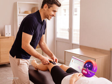 Physiotherapeut behandelt Patientin am Knie. Im Vordergrund NOVENTI Ora Character mit Screenshot aus NOVENTI Ora.