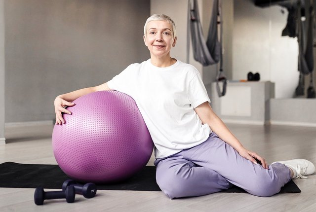 Trainerin beim Rehasport mit Medizinball sitzend auf Sportmatte