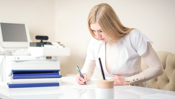 Medizinische Fachkraft füllt ein Formular am Schreibtisch aus – Symbolbild für die Positionierung und Taxierung auf der Heilmittelverordnung Muster 13 in der Physiotherapie.
