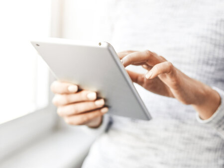 Therapeutin, die am Fenster steht und den Bildschirm eines digitalen Tablets berührt. – Symbolbild für Hilfsmittelverzeichnis – Alle Infos