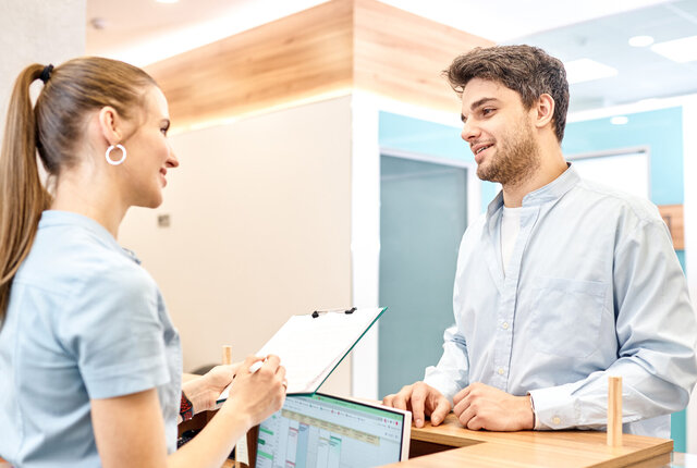 Physiotherapeuten spricht mit einem Patienten an der Rezeption – Symbolbild für Blogbeitrag Die größten Effizienz-Fallen im Praxisalltag