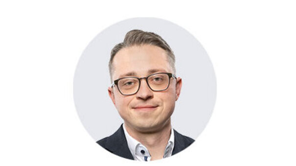 Porträtaufnahme von Sales Manager Steffen Kreisig mit kurzer Frisur, Brille und dunklem Blazer vor neutralem, hellem Hintergrund.