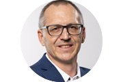 Porträtaufnahme von Sales Manager Dirk Geitner mit kurzer Frisur, Brille und dunklem Sakko vor neutralem, hellem Hintergrund.